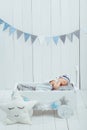 cute newborn baby in hat sleeping in wooden baby cot with star pillow