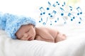 Cute newborn baby in knitted hat sleeping on bed and flying music notes.