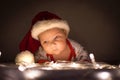 Cute newborn baby with santa hat raised his head over the lights under christmas tree Royalty Free Stock Photo