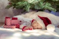 Cute newborn baby sleeping under Christmas tree near red gifts wearing Santa Claus hat Royalty Free Stock Photo