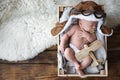 Cute newborn baby wearing aviator hat with toy sleeping in wooden crate. Space for text