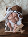 Cute newborn baby wearing aviator hat with toy sleeping in wooden crate