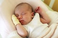 Cute newborn baby with yellow mitten on a hand is sleeping on her bed under beige blanket Royalty Free Stock Photo