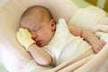 Cute newborn baby with yellow mitten on a hand is sleeping on her bed under beige blanket Royalty Free Stock Photo