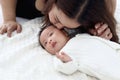 Cute newborn infant baby boy lying down on white on bed in white bedroom, mother gentle touching and kissing him, lovely family