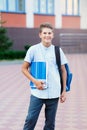 Cute, nice, young 11 years old boy in blue shirt stands with workbooks and backpack in front of his school. Education Royalty Free Stock Photo