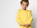 cute obedient preschool girl, modestly posing on a light background in a yellow hoodie with a hood