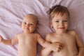 Cute older brother holding his little sister by the hand while lying on the lilac sheet