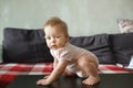 Cute one year infant sitting on a table at home room, getting ready to stand up