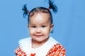 Cute one year old mixed race Asian Caucasian german girl wearing red dress smiles sweetly looking at the camera on blue background Royalty Free Stock Photo