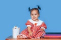 Cute one year old mixed race Asian Caucasian german girl wearing red dress smiles sweetly looking at the camera on blue background Royalty Free Stock Photo