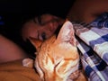 Cute orange cat sleeping in bed with human. Ginger kitty relaxing with female owner in dark room at home. Soft focus Royalty Free Stock Photo