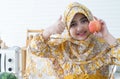 Cute Pakistani little Muslim girl in traditional clothes and hijab standing and enjoy with red apple in hand at home kitchen, Royalty Free Stock Photo
