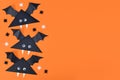 Cute paper vampire bats with funny googly eyes on side of orange Halloween background with copy space