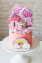 Cute pink birthday cake for a little girl with fondant unicorn, gingerbread princess castle, rainbow and meringue