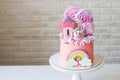 Cute pink birthday cake for a little girl with fondant unicorn, gingerbread princess castle, rainbow and meringue