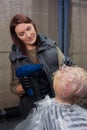 Cute and pleasant brunette, adult girl, European hairdresser, in the process of work, dries the hair of a client in a barbershop