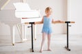 Cute plump ballerina in a blue leotard is doing ballet dancing at the ballet barre in a large bright classroom
