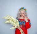 Cute plump girl from the village in a red summer sundress with a sheaf of wheat in her hands on white studio solid background