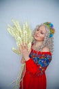 Cute plump girl from the village in a red summer sundress with a sheaf of wheat in her hands on white studio solid background