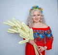 Cute plump girl from the village in a red summer sundress with a sheaf of wheat in her hands on white studio solid background