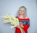 Cute plump girl from the village in a red summer sundress with a sheaf of wheat in her hands on white studio solid background