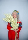 Cute plump girl from the village in a red summer sundress with a sheaf of wheat in her hands on white studio solid background