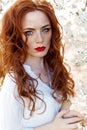 Cute portrait of a beautiful redhead girl with make-up and red lipstick in a white shirt in the garden among the blooming trees on