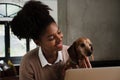 Cute portrait of female teen playing with cute pupping sitting in front on laptop in modern kitchen Royalty Free Stock Photo