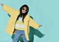 Cute positive chinese brunette girl in stylish yellow furry coat, jeans and sunglasses feeling like flying