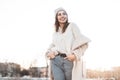 Cute positive young woman with beautiful smile in a fashionable knitted warm hat in a stylish milk-colored fur coat made of faux Royalty Free Stock Photo