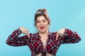 Cute positive young woman in a plaid shirt and bandage poses on a blue background and shows her fingers down. Concept of Royalty Free Stock Photo