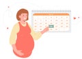 Cute pregnant girl stands by the monthly planner calendar. Woman points to the calendar with her hand