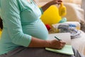 Cute Pregnant Woman writing packing list for maternity hospital With Notebook Prepares bags. Young Ledy In Pregnancy Royalty Free Stock Photo