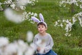 Cute preschool boy with bunny ears in garden. smiling child siting on green lawn against background of trees blooming