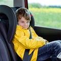 Cute preschool kid boy sitting in car in yellow rain coat. Little school child in safety car seat with belt enjoying Royalty Free Stock Photo