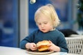 Cute preschooler boy eating large hamburger at fast food restaurant. Unhealthy meal for kids. Junk food. Overweight problem child