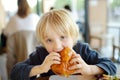 Cute preschooler boy eating large hamburger at fast food restaurant. Unhealthy meal for kids. Junk food. Overweight problem child