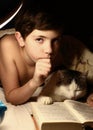 Cute preteen boy with book lamp and cat in bed