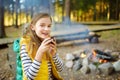 Cute preteen girl drinking tea and roasting marshmallows on stick at bonfire. Child having fun at camp fire. Camping with children Royalty Free Stock Photo