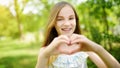Cute preteen girl laughing and holding her hands in a heart shape on bright and sunny summer day. Cute child enjoying herself outd Royalty Free Stock Photo