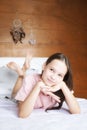 Cute preteen girl in pink t-shirt dreaming on white bed in boho style room against wooden wall and dreamcatchers. Scandinavian in