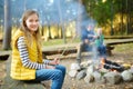 Cute preteen girl roasting hotdog on a stick at bonfire. Child having fun at camp fire. Camping with kids in fall forest.
