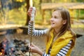 Cute preteen girl roasting marshmallows on stick at bonfire. Child having fun at camp fire. Camping with children in fall forest.