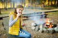 Cute preteen girl roasting marshmallows on stick at bonfire. Child having fun at camp fire. Camping with children in fall forest.