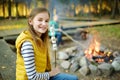 Cute preteen girl roasting marshmallows on stick at bonfire. Child having fun at camp fire. Camping with children in fall forest.