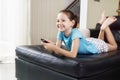 Cute preteen girl watching TV on couch using remote control. Living room interior in background