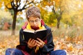 Cute pretty boy in costume of Harry Potter and scarf plays as a magician, reads book in autumn