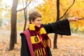 Cute pretty boy in costume of Harry Potter and scarf plays as a magician, reads book in autumn