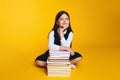 Cute pupil girl wearing school uniform, holding hand under chin while sitting near pile of books Royalty Free Stock Photo